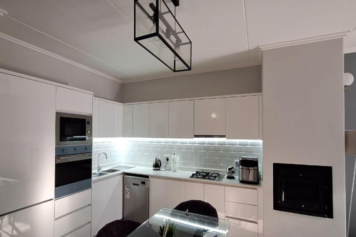 Modern kitchen featuring high-gloss white cabinetry, subway tile backsplash, integrated appliances, and a sleek black pendant light, adjacent to a built-in fireplace.