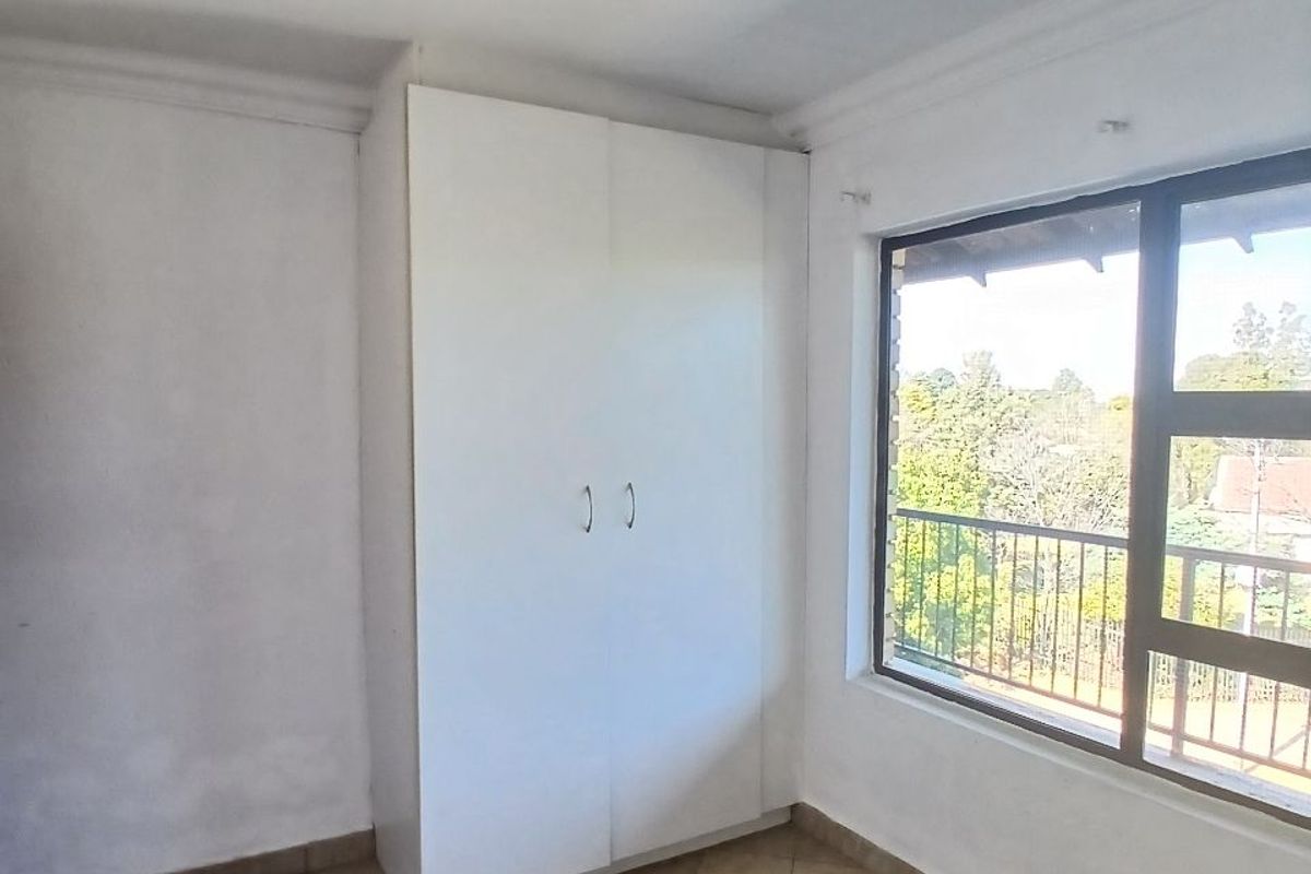 A bright, empty bedroom featuring tiled flooring, a built-in wardrobe, and a large window with views of the surrounding area.