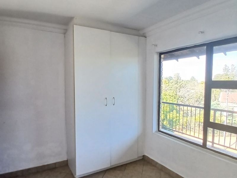 A bright, empty bedroom featuring tiled flooring, a built-in wardrobe, and a large window with views of the surrounding area.