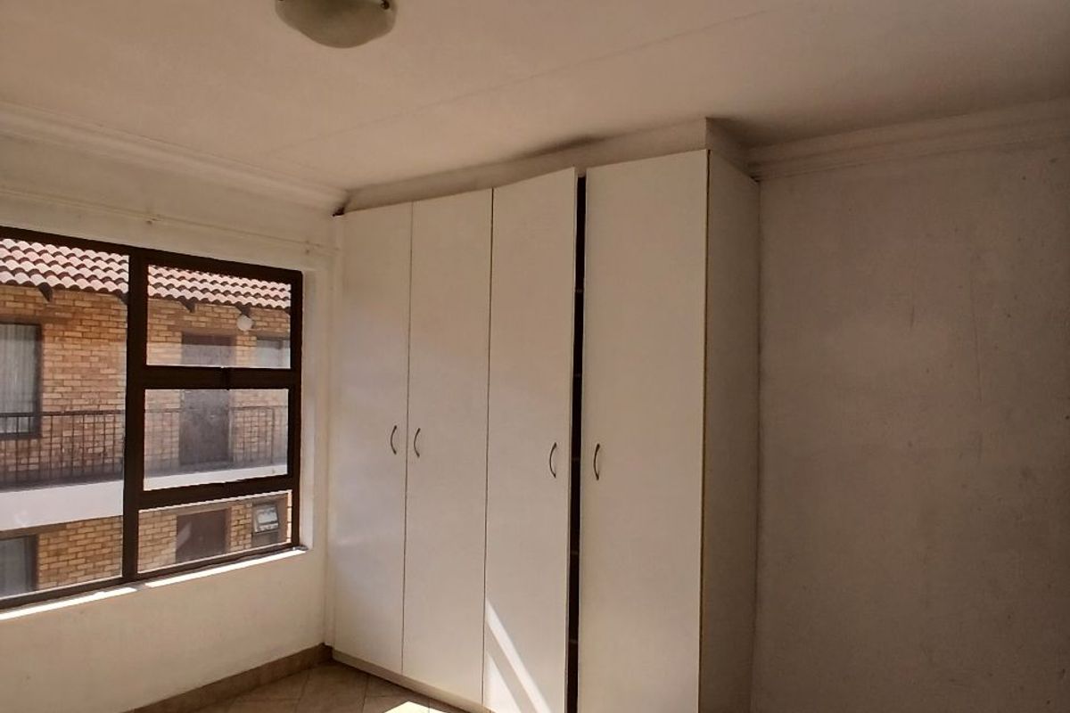 A bright, empty bedroom featuring tiled flooring and a built-in white wardrobe, offering a clean canvas for personalization.