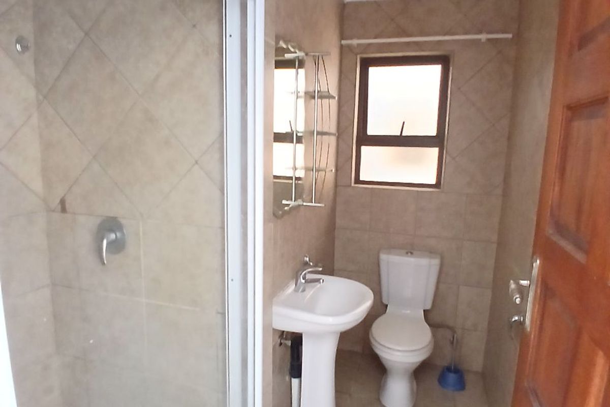 A functional bathroom featuring a shower enclosure, pedestal basin, and toilet with neutral wall and floor tiling.
