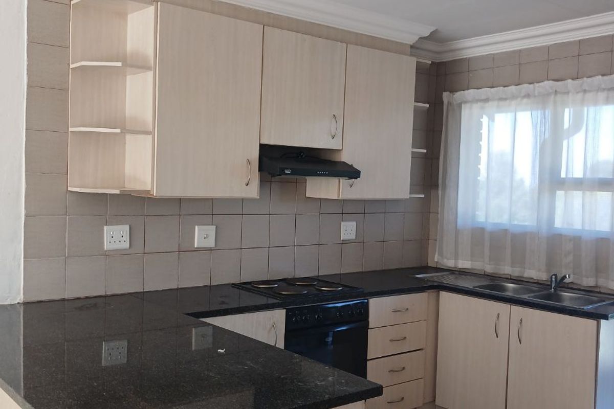 A functional kitchen featuring granite countertops, built-in cabinetry, an electric hob with extractor fan, and a double basin sink with tiled backsplash.