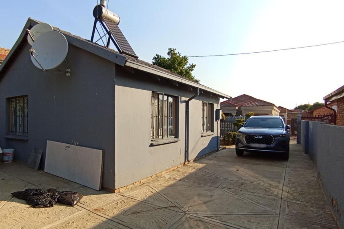 Rear exterior view of the property featuring a paved driveway, perimeter wall, and solar water heating system installed on the roof.