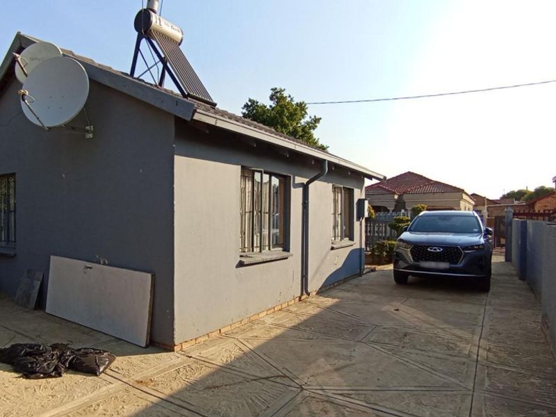 Rear exterior view of the property featuring a paved driveway, perimeter wall, and solar water heating system installed on the roof.