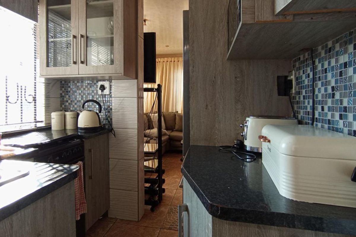 Compact kitchen featuring wood-look laminate cabinetry, mosaic tile backsplash, and dark countertops, with a direct view into the adjacent living area.