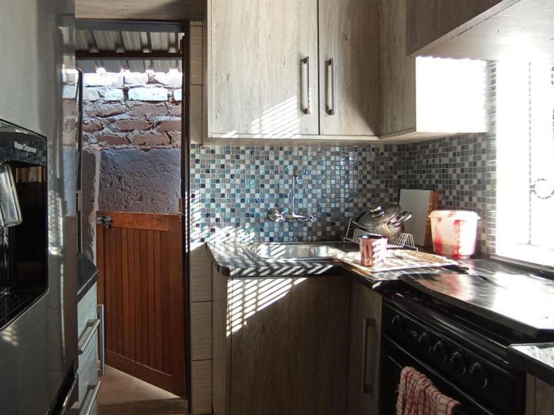 Compact kitchen featuring wood-look cabinetry, mosaic tile backsplash, and direct access to an outdoor area.