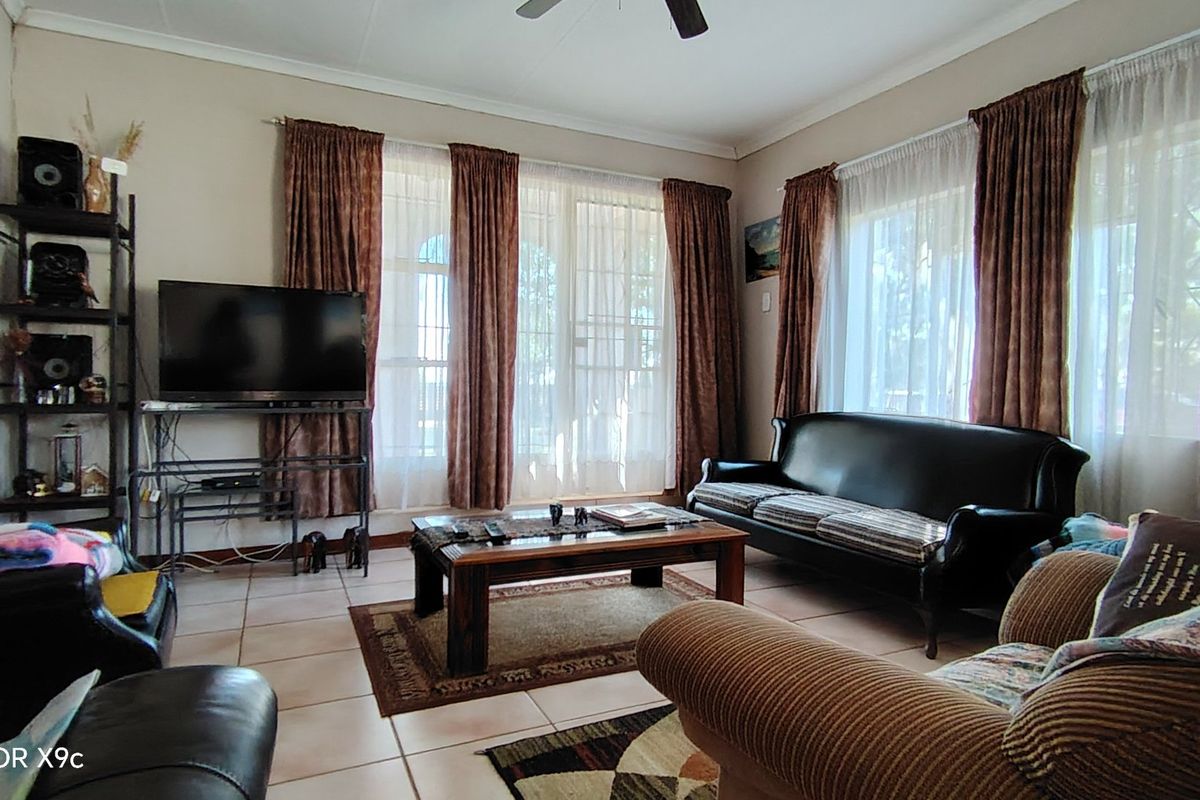A comfortable living room featuring tiled flooring, a ceiling fan, and large windows with security gates, providing a bright and functional space.