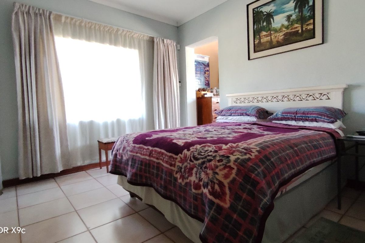 A bedroom featuring tiled flooring and a large window with curtain rails, providing natural light.