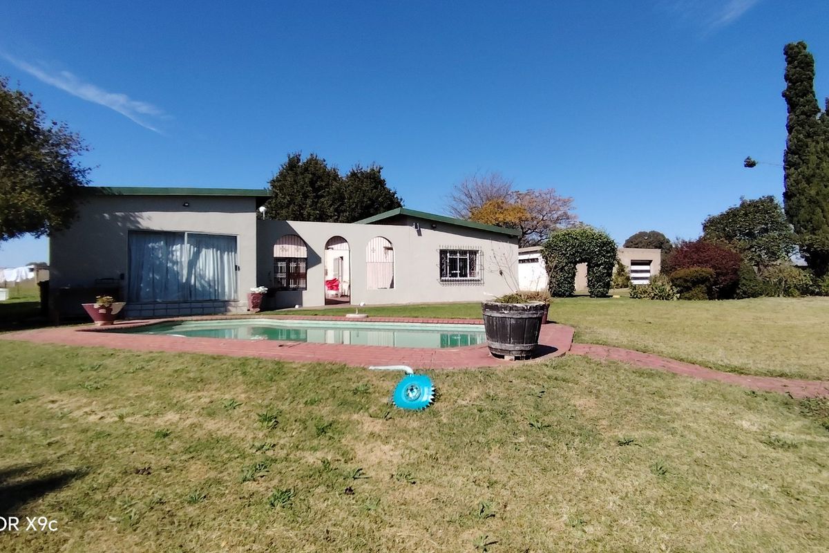Rear view of the farmhouse featuring a swimming pool, brick paved surround, and established garden area with mature trees.