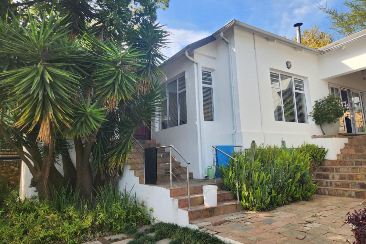 Rear exterior view of the house featuring a tiled staircase with stainless steel handrails leading to the entrance, set against a landscaped garden.