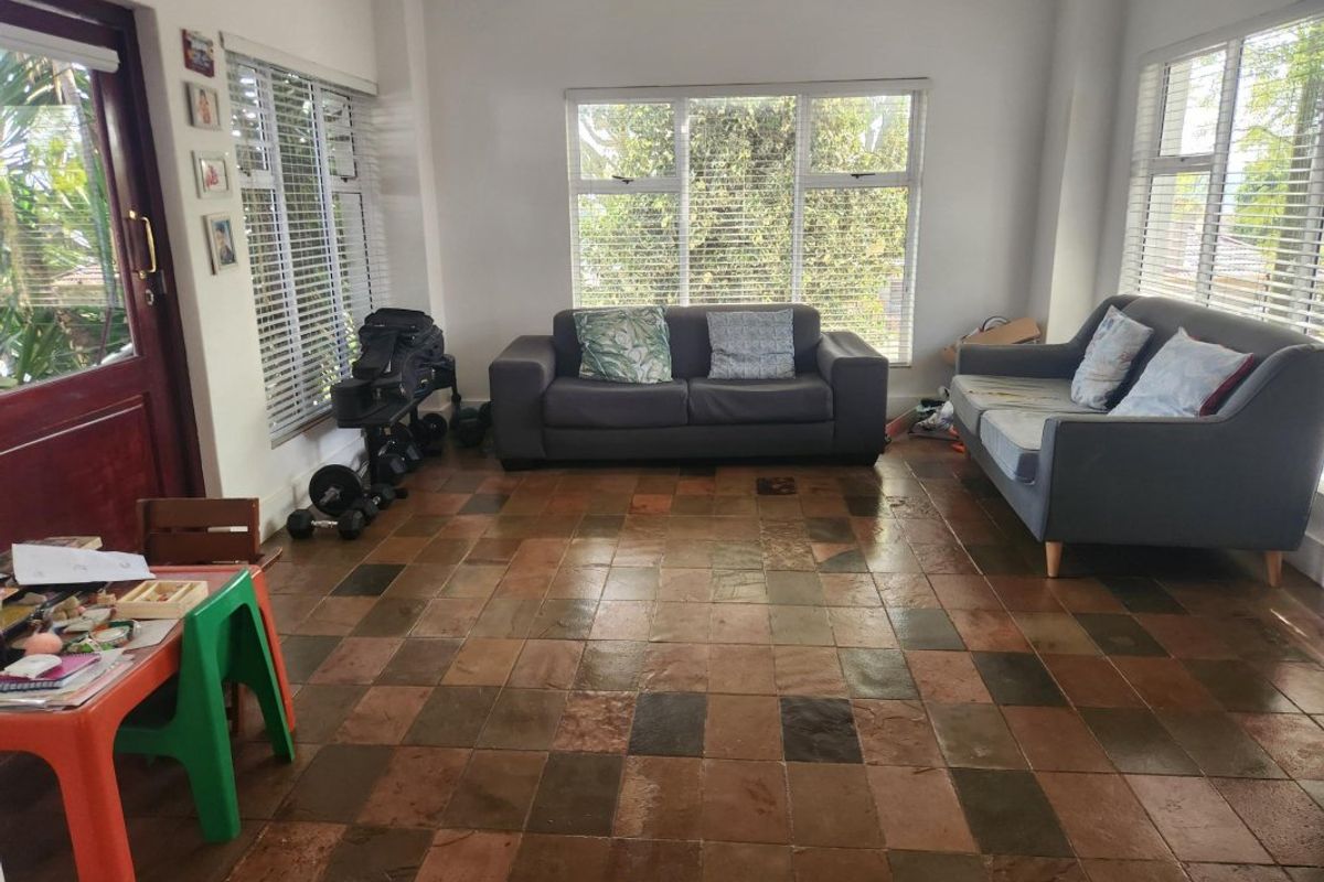 A sunlit living room featuring natural slate tile flooring, large windows with venetian blinds, and direct access to the exterior.