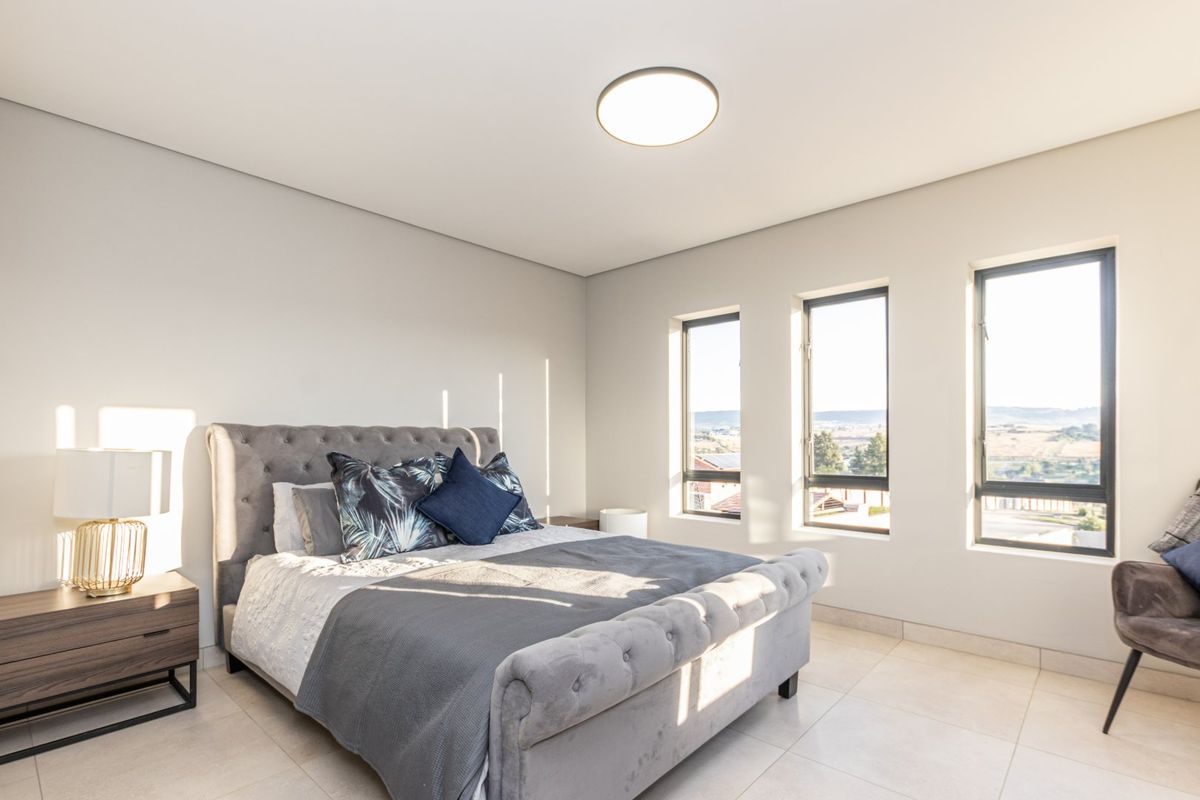 A bright and modern bedroom featuring neutral tiled flooring, contemporary recessed lighting, and large aluminium-framed windows offering scenic views.