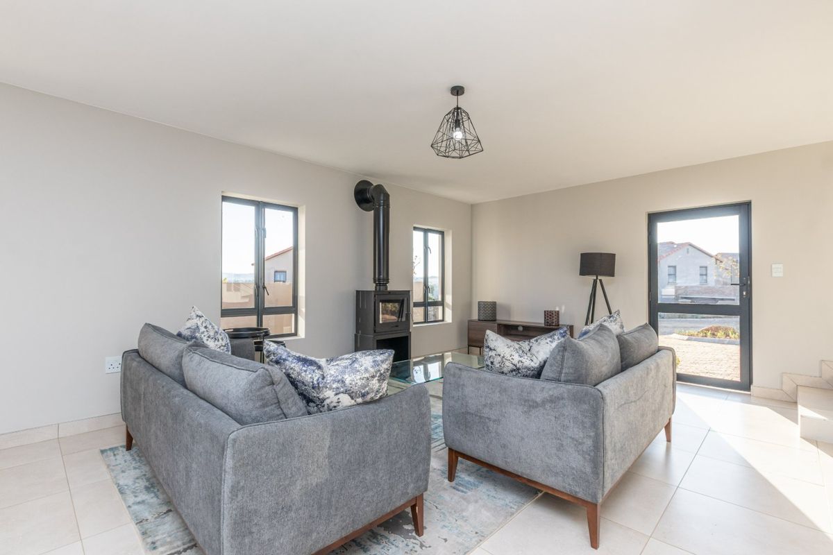 A bright and modern living room featuring tiled floors, a contemporary freestanding fireplace, and large aluminium-framed windows and doors providing natural light.