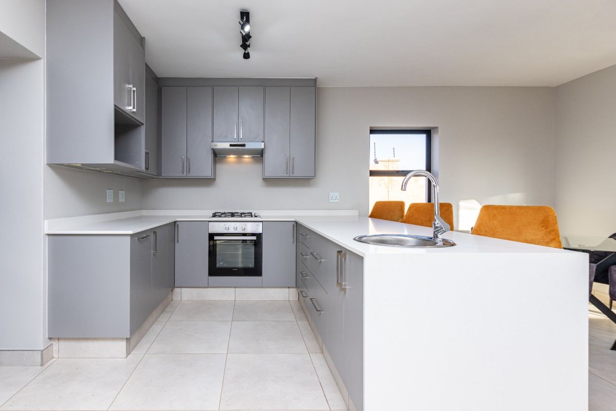 Modern kitchen featuring sleek grey cabinetry, white stone countertops, built-in oven, gas hob, and a functional island with a stainless steel sink.