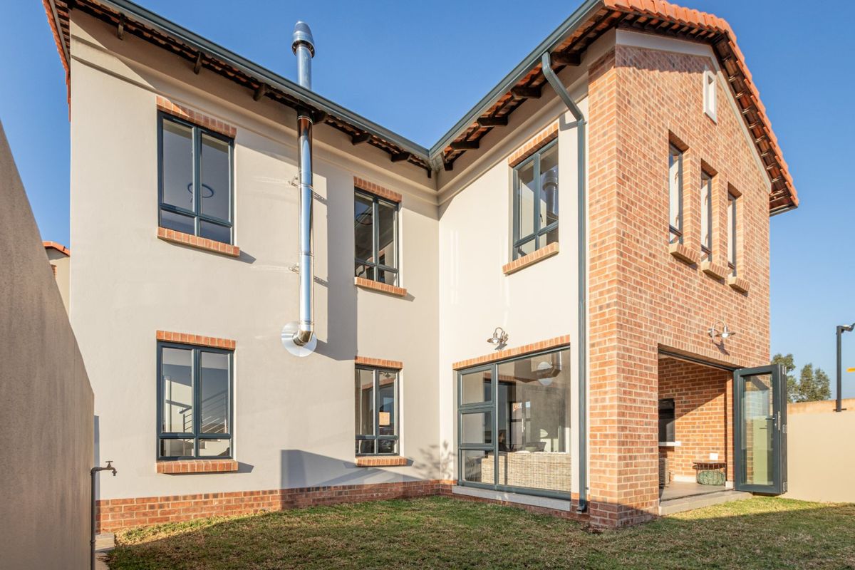 Rear view of a modern townhouse featuring a combination of brick and plastered finishes, a covered patio area, and an external fireplace flue.