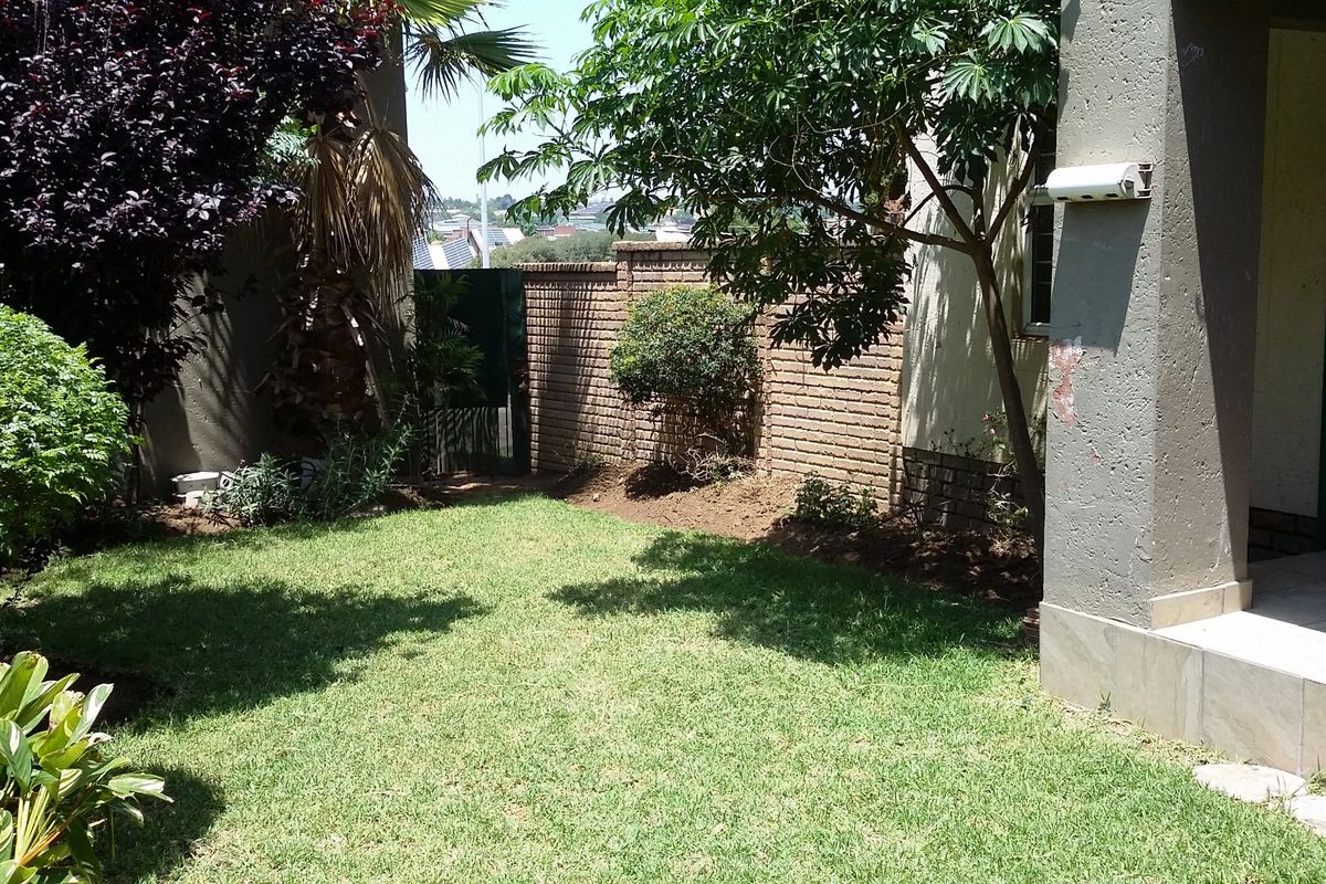 A private rear garden featuring a manicured lawn, established trees, and a brick boundary wall, adjacent to a tiled patio area.