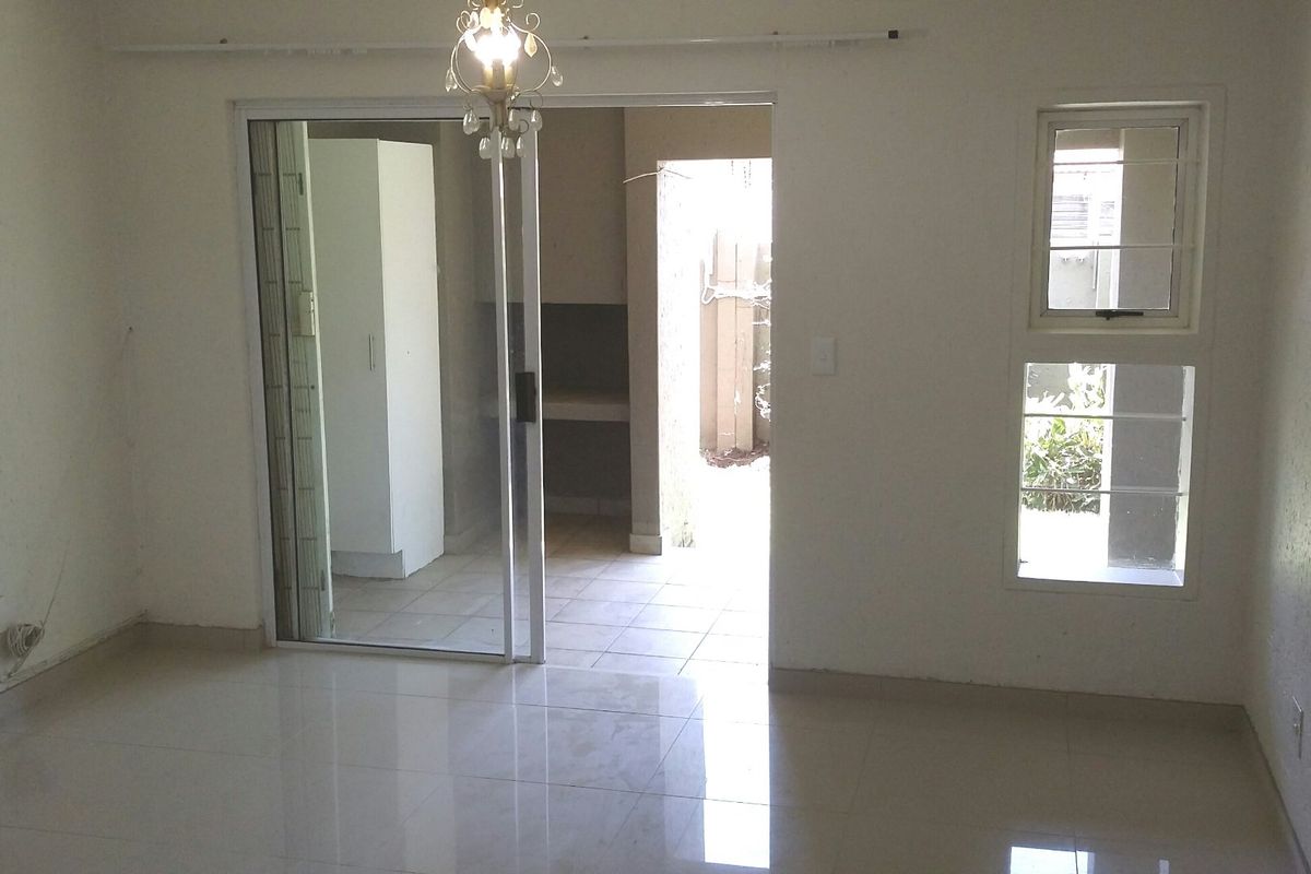 An empty living room featuring tiled flooring, a sliding glass door leading to an outdoor area, and security bars on the windows.
