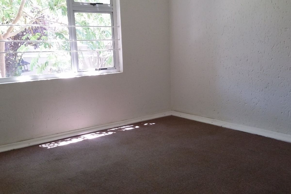 An empty bedroom featuring carpet flooring, white textured walls, and an aluminium window with security bars.