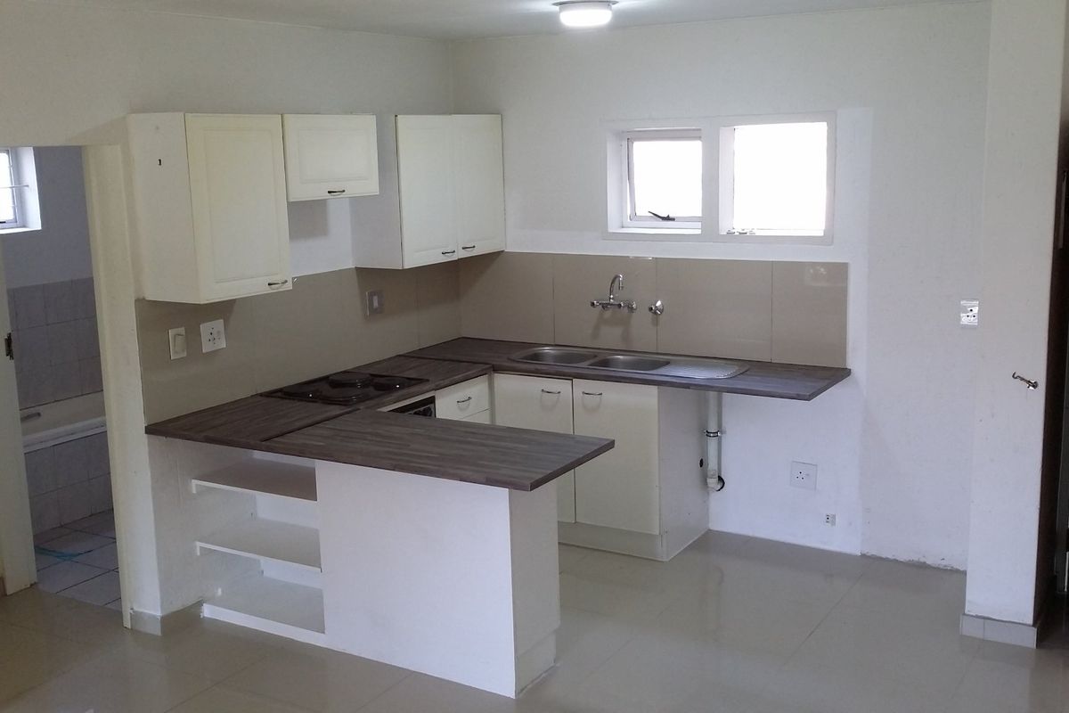 A functional, empty kitchen featuring white cabinetry, dark laminate countertops, a built-in hob, and tiled flooring, ready for personalization.