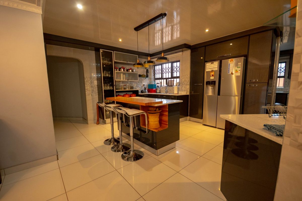 Modern kitchen featuring high-gloss cabinetry, a central island with breakfast bar seating, stone countertops, and integrated lighting.