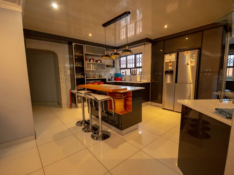 Modern kitchen featuring high-gloss cabinetry, a central island with breakfast bar seating, stone countertops, and integrated lighting.