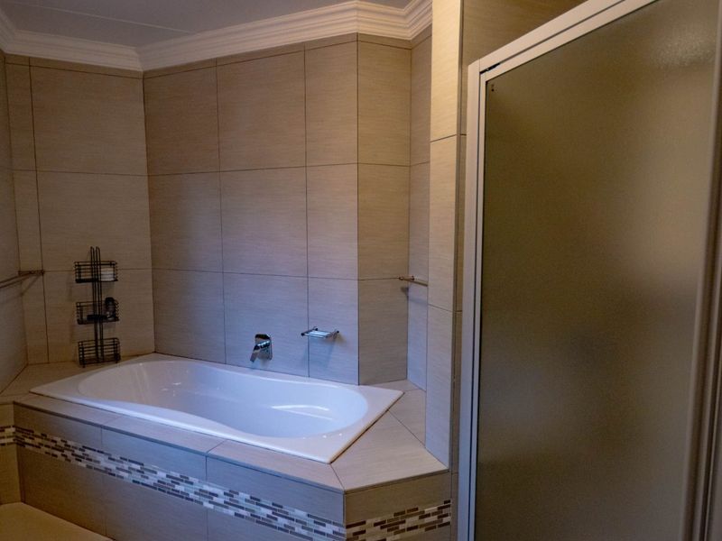 A well-maintained bathroom featuring a built-in bathtub with decorative tile accents, a separate shower enclosure, and neutral wall tiling.