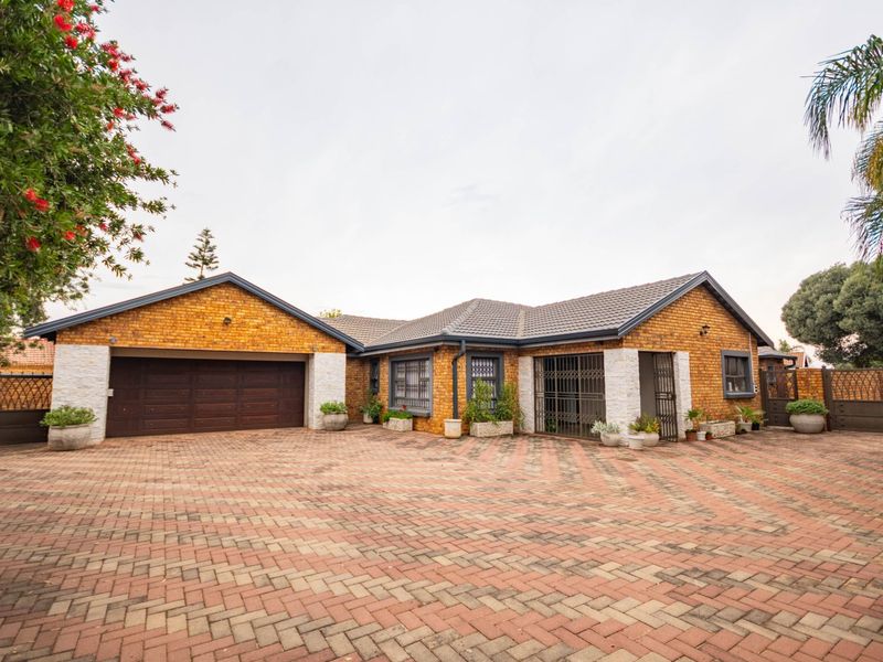 Front view of a well-maintained face brick house featuring a spacious paved driveway, double garage, and secure entrance.