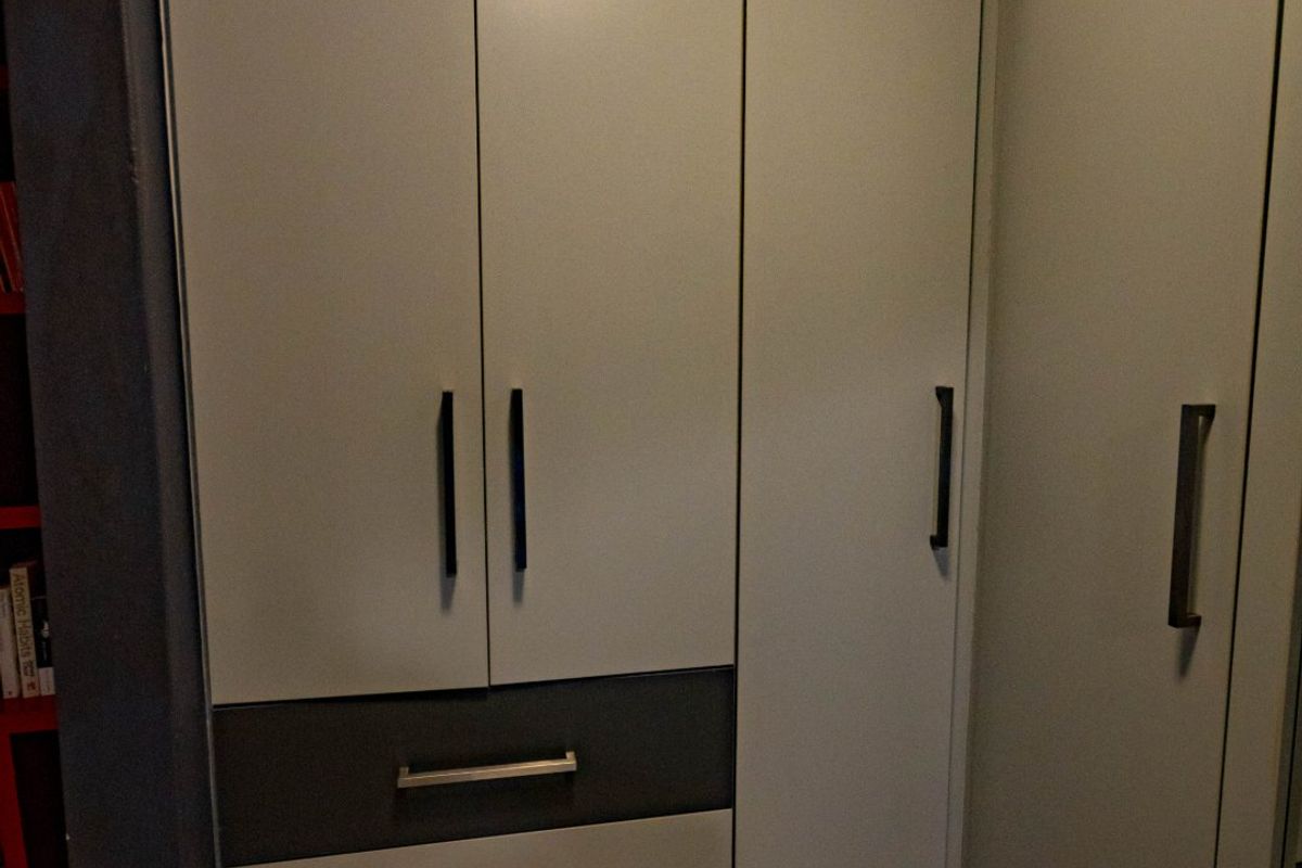 A bedroom featuring modern, neutral-toned built-in cupboards with integrated drawers and clean tiled flooring.