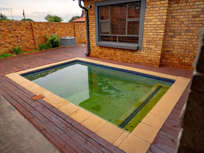 Outdoor pool area featuring timber decking, brick boundary walls, and a tiled roof structure.