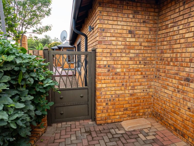 A side access area featuring face brick walls, a secure metal gate, and durable paved flooring leading to the rear of the property.