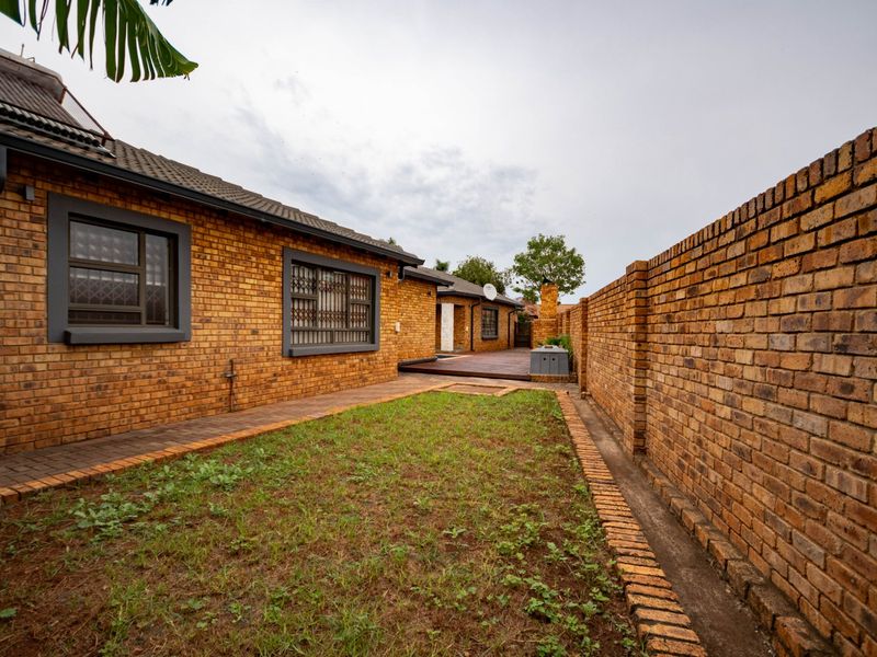 A rear exterior view of the property featuring face brick walls, a paved walkway, and a timber deck area.
