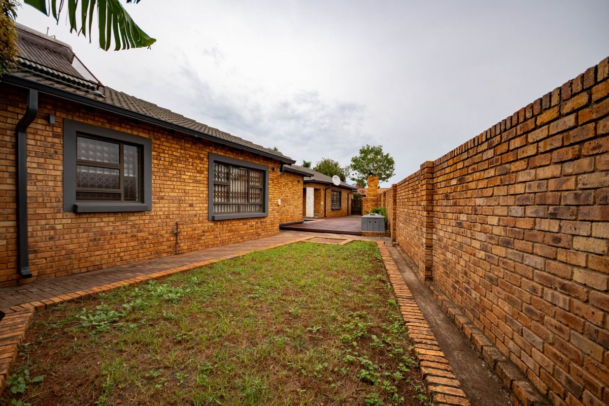 A rear exterior view of the property featuring face brick walls, a paved walkway, and a timber deck area.