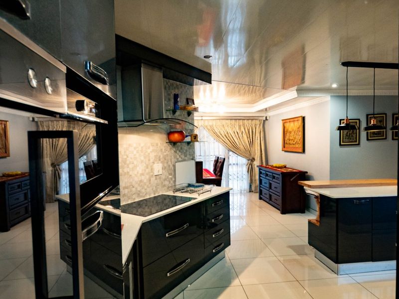 Modern open-plan kitchen featuring high-gloss cabinetry, integrated appliances, a central island, and polished tiled flooring, seamlessly flowing into the adjacent living area.