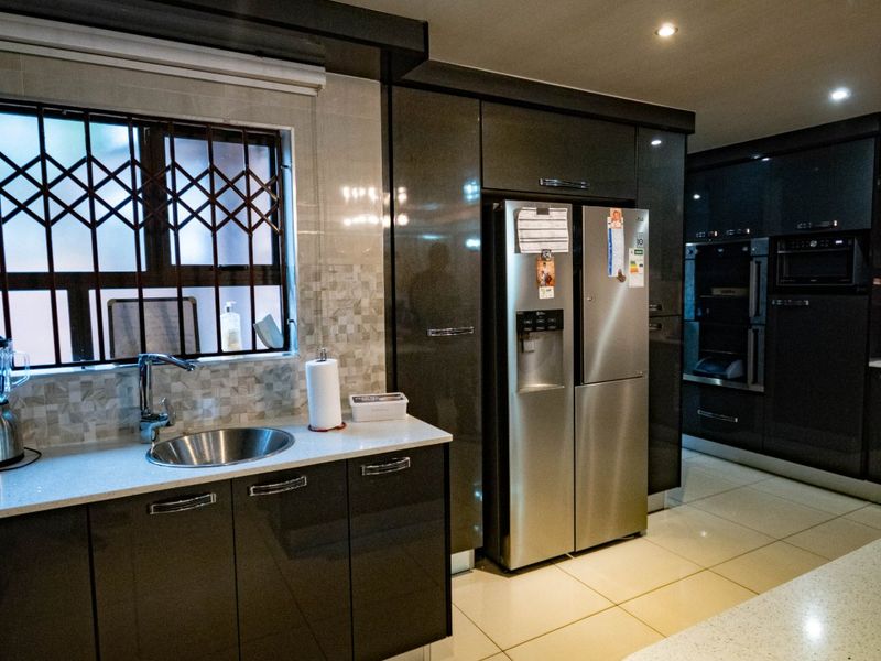 Modern kitchen featuring high-gloss cabinetry, stone countertops, integrated appliances, and tiled flooring with a window security gate.