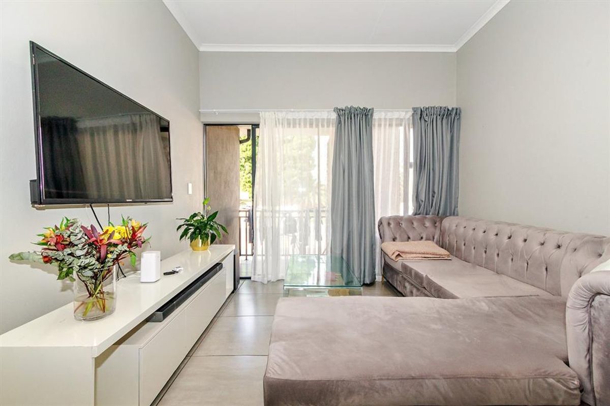 A well-maintained living room featuring large format floor tiles, coved ceilings, and a sliding glass door providing access to an outdoor balcony area.