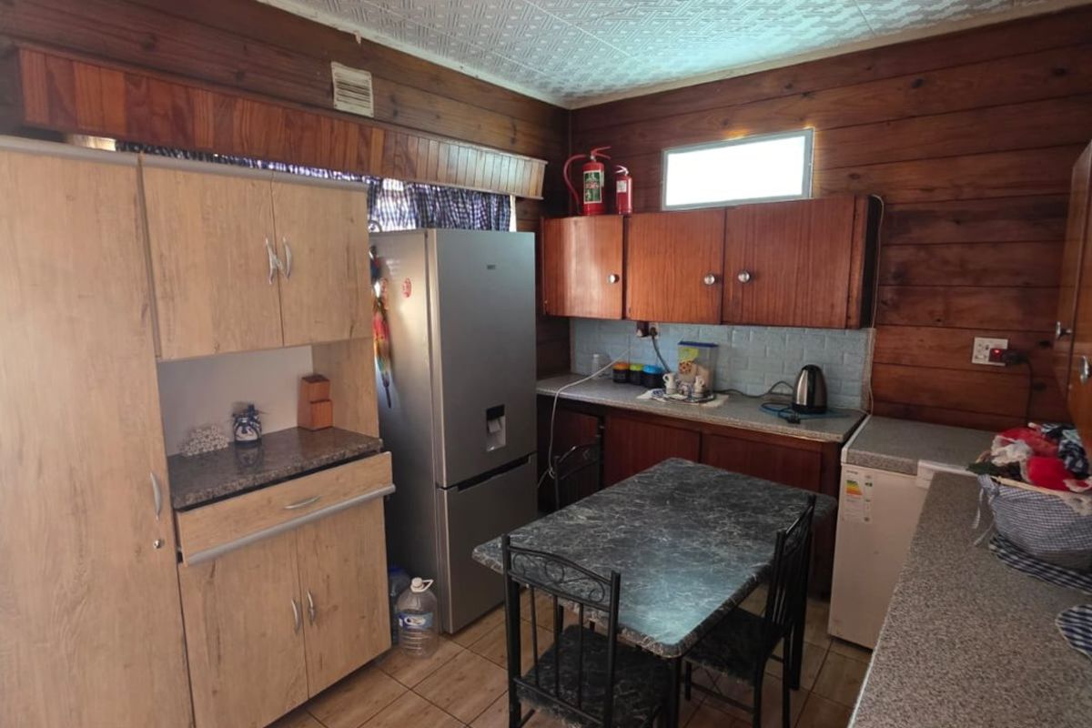 A dated kitchen featuring timber wall paneling, textured ceiling tiles, tiled flooring, and a mix of laminate cabinetry and countertops.