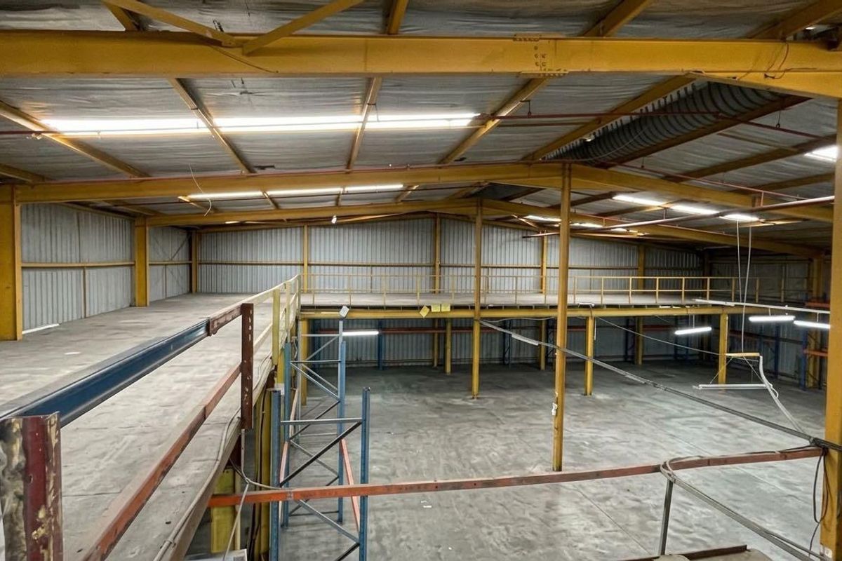 Spacious industrial warehouse featuring a steel mezzanine level, high ceilings with exposed portal frame, concrete flooring, and functional overhead lighting.