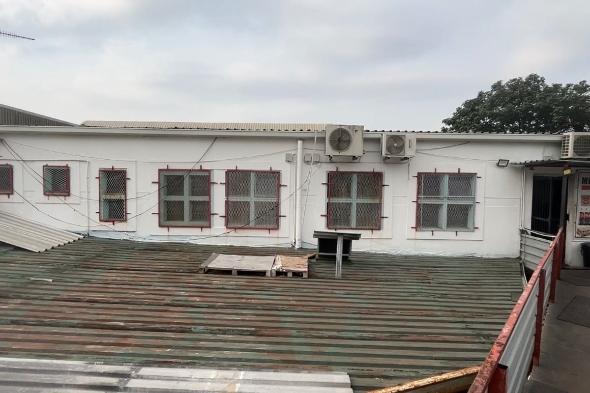 Rear exterior view of the industrial building featuring a corrugated metal roof, security-grille windows, and external air conditioning units.
