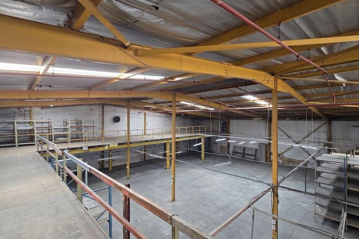 Spacious industrial warehouse featuring a mezzanine level, exposed steel roof trusses, concrete flooring, and an integrated fire sprinkler system.