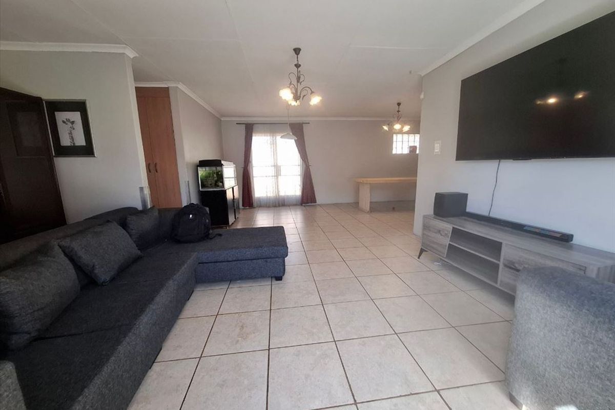 Spacious open-plan living area featuring neutral wall tones, tiled flooring, and natural light from the rear window.