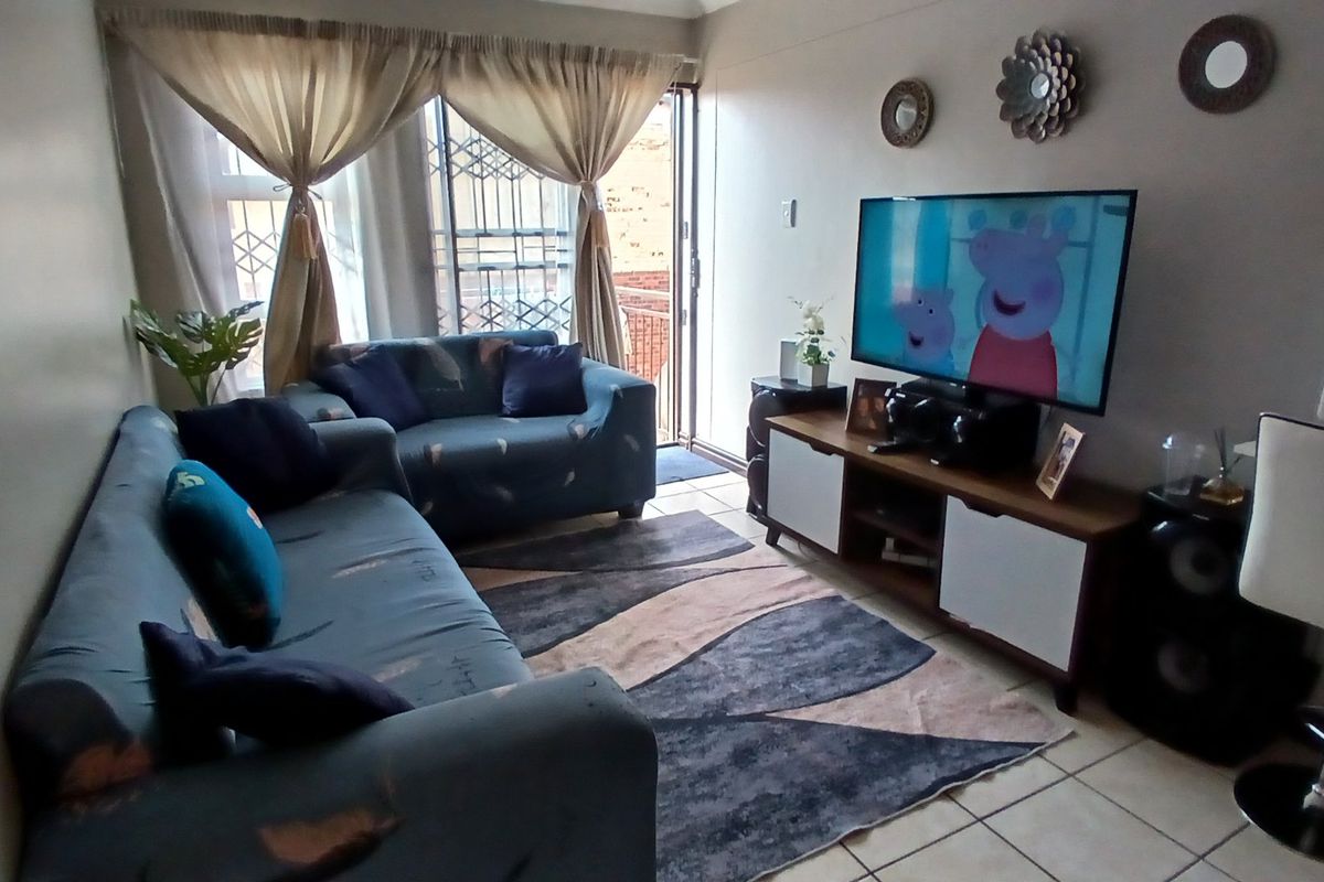 A comfortable living room featuring tiled flooring and a sliding glass door with security gate, providing access to an outdoor area.