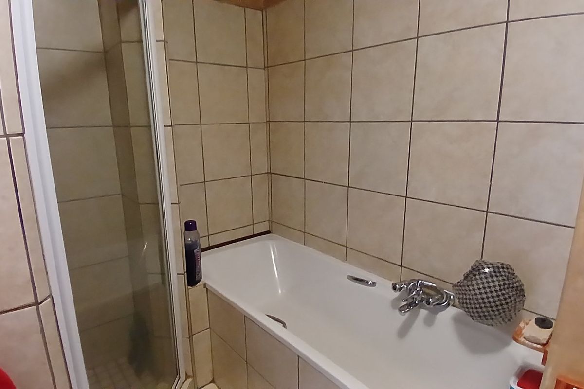 A functional bathroom featuring a tiled shower enclosure and a standard bathtub with chrome fixtures, presenting a dated but well-maintained aesthetic.