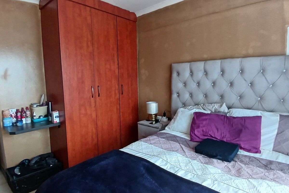 A bedroom featuring a built-in wooden wardrobe and an exposed electrical distribution board on the wall, which shows signs of surface staining.