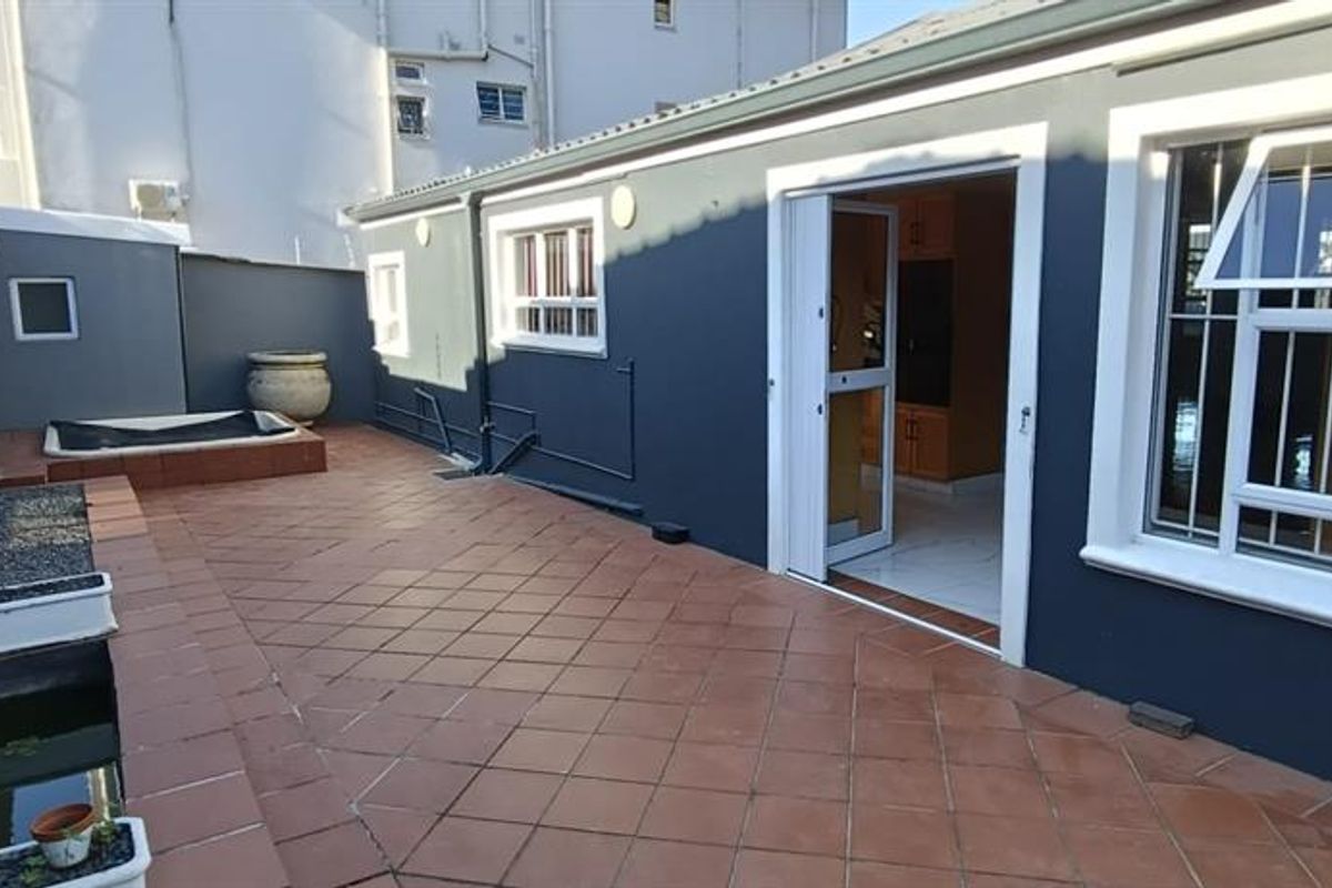 A paved rear patio area featuring a built-in water feature, raised planter, and direct access to the interior through a sliding door.