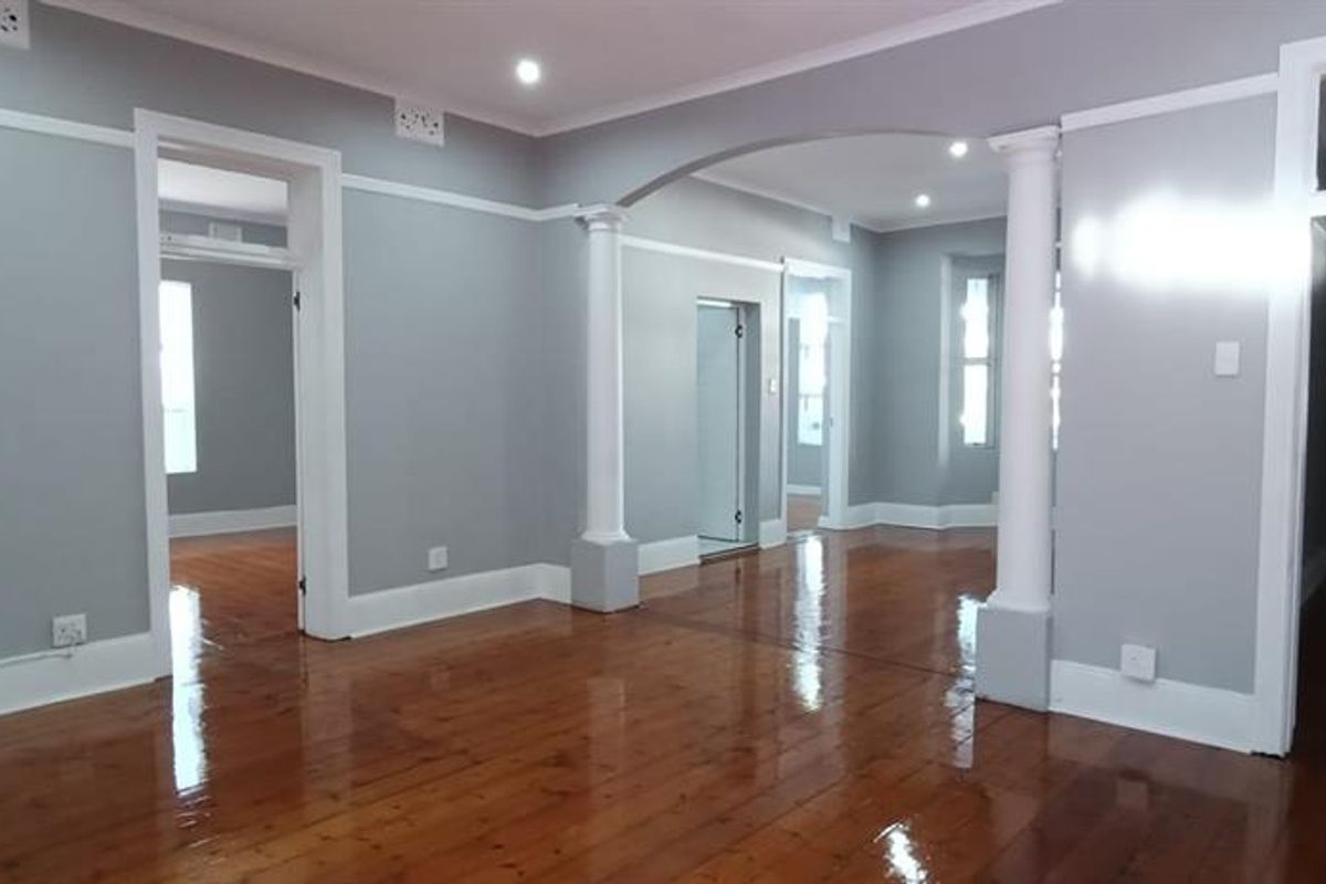 Spacious, empty living area featuring polished timber floors, decorative columns, and an open-plan layout with neutral grey walls and classic architectural detailing.