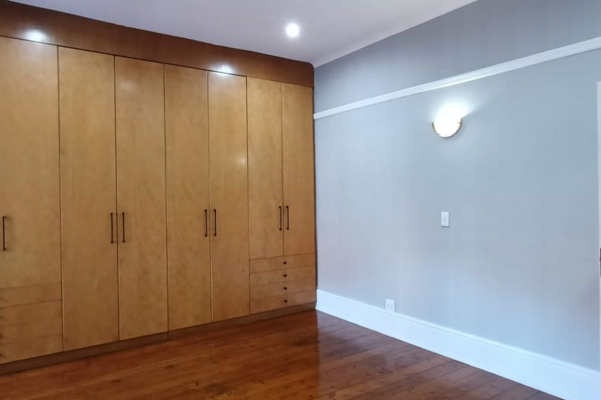 A spacious bedroom featuring polished hardwood flooring, extensive built-in wooden cabinetry, and neutral wall finishes with classic architectural detailing.