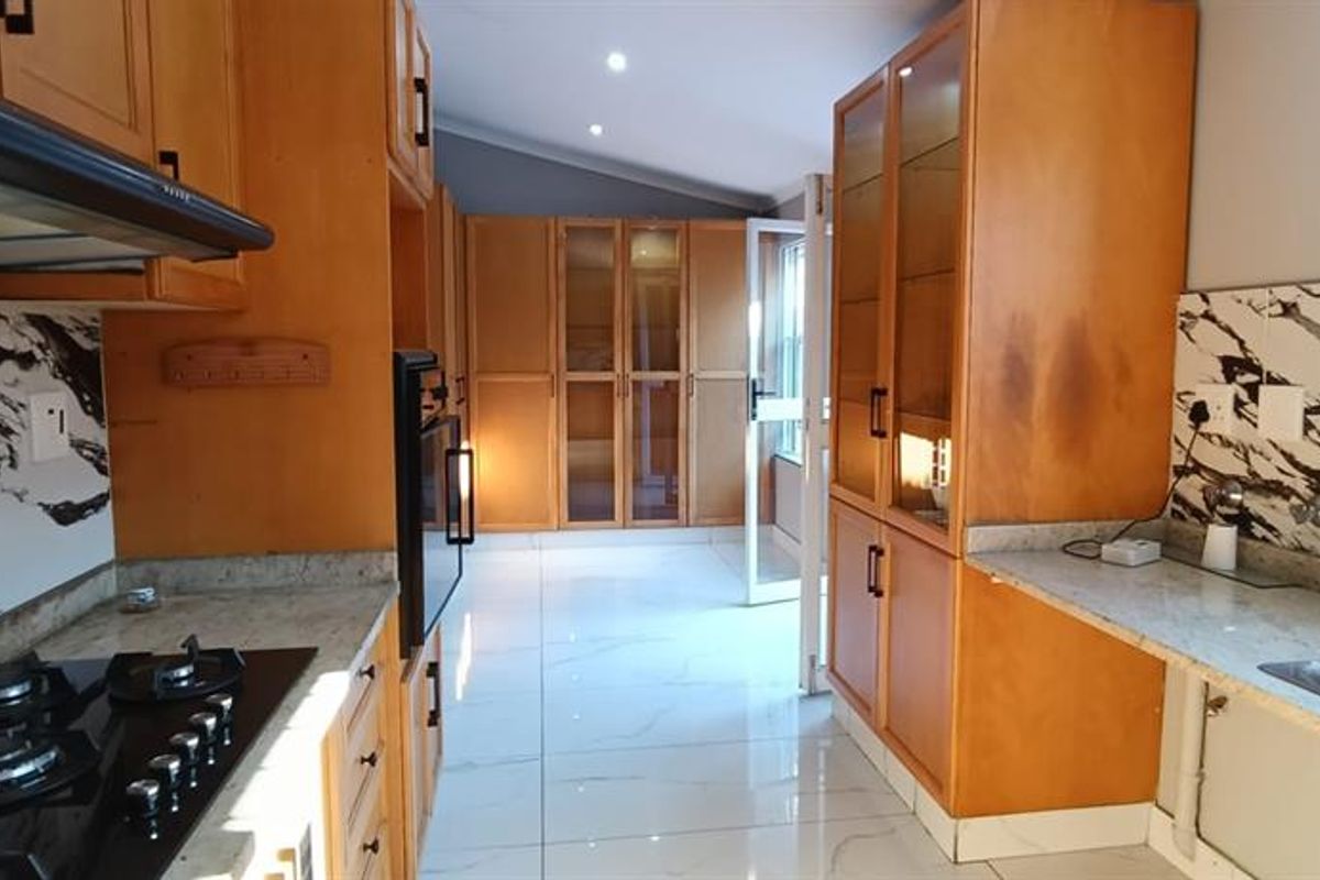 A well-maintained kitchen featuring wooden cabinetry, stone countertops, a gas hob with extractor, and modern marble-look splashbacks with tiled flooring.