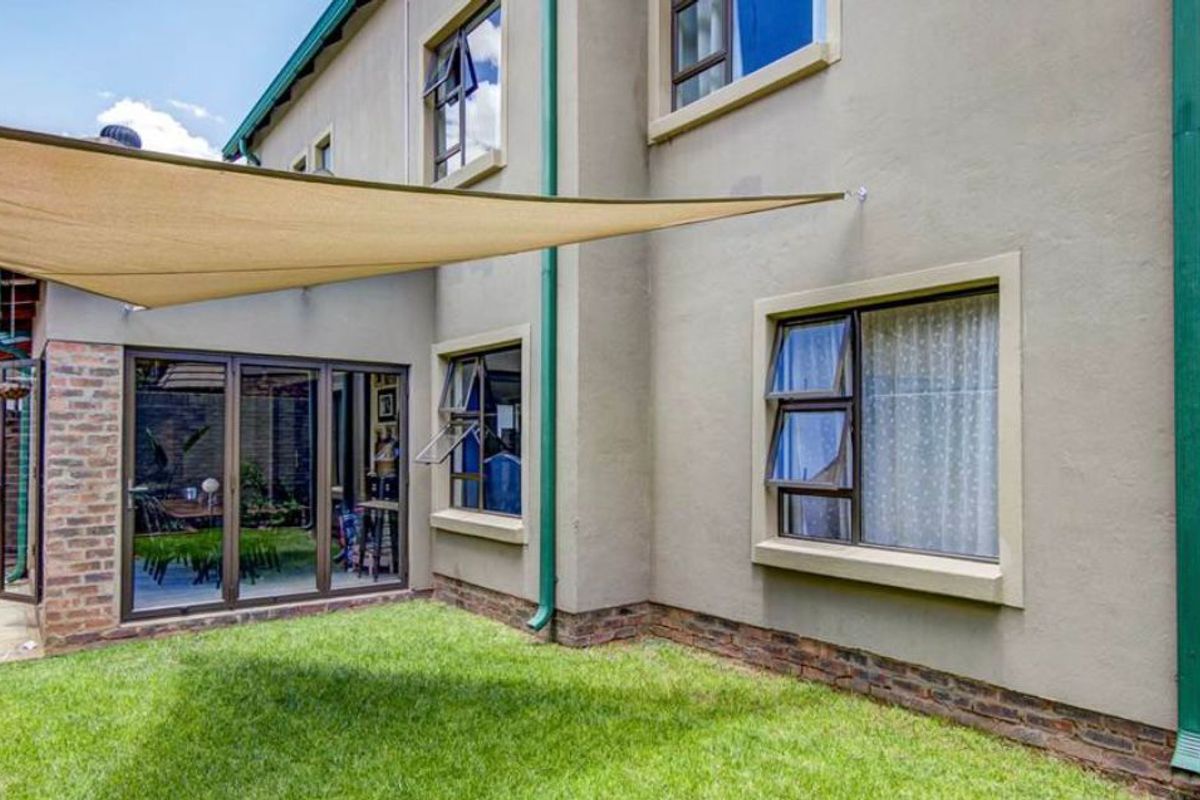 Rear exterior view of the house featuring a lawn, paved walkway, shade sail, and aluminium framed windows and sliding doors.