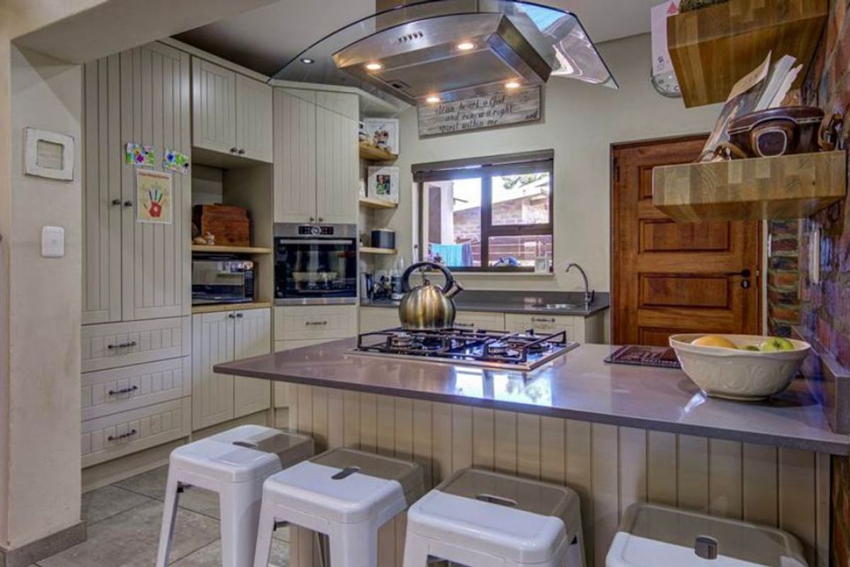 A well-appointed kitchen featuring shaker-style cabinetry, stone countertops, a central gas hob with extractor, and a charming exposed brick feature wall.
