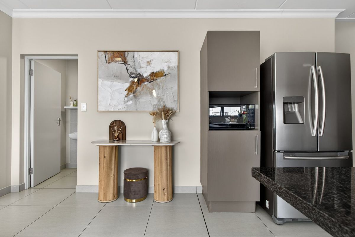 A modern kitchen area featuring sleek cabinetry with built-in microwave housing, granite countertops, and neutral tiled flooring, leading to an adjacent room.